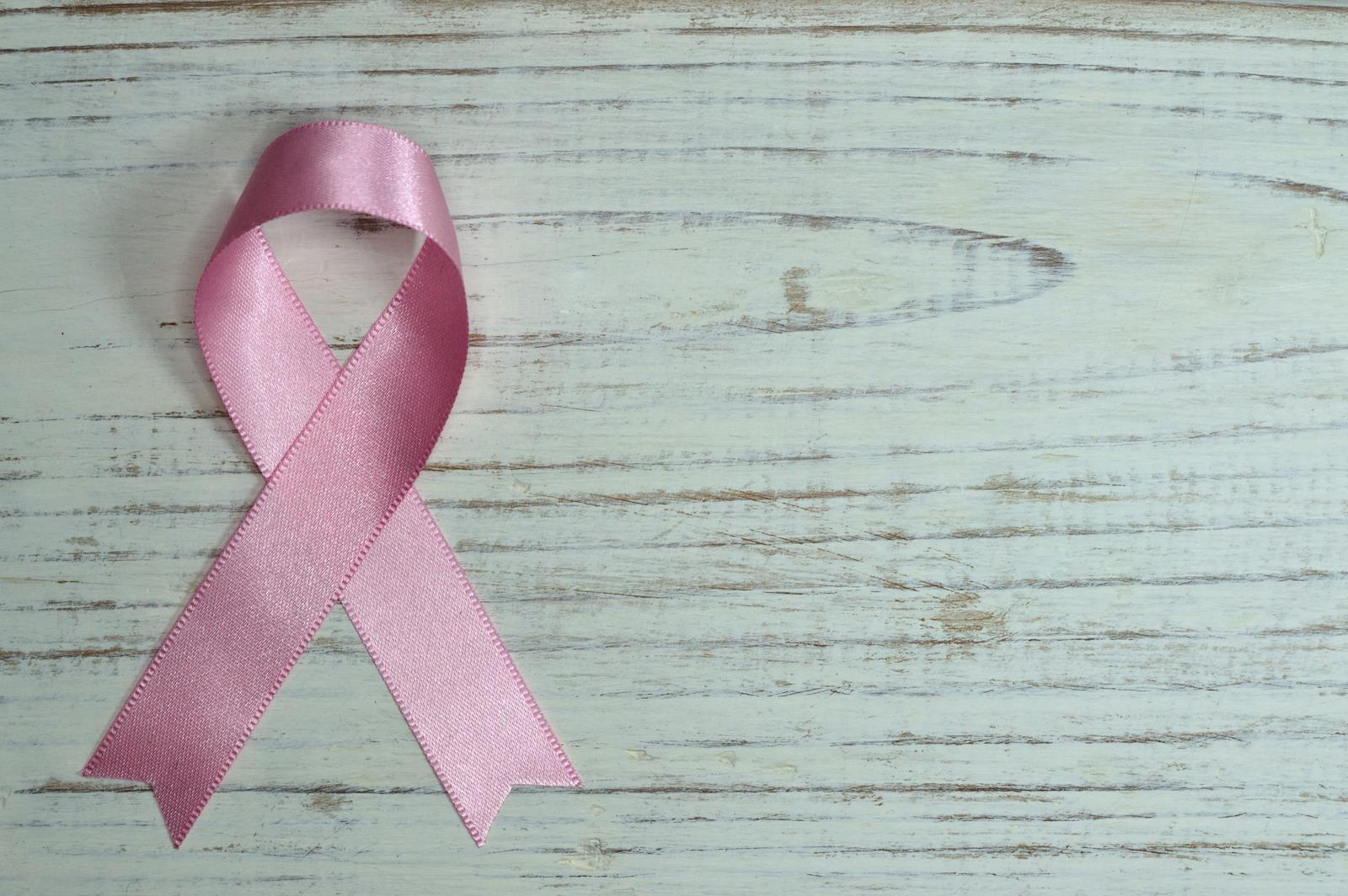 A pink ribbon symbolizing cancer awareness placed on a light wooden background.