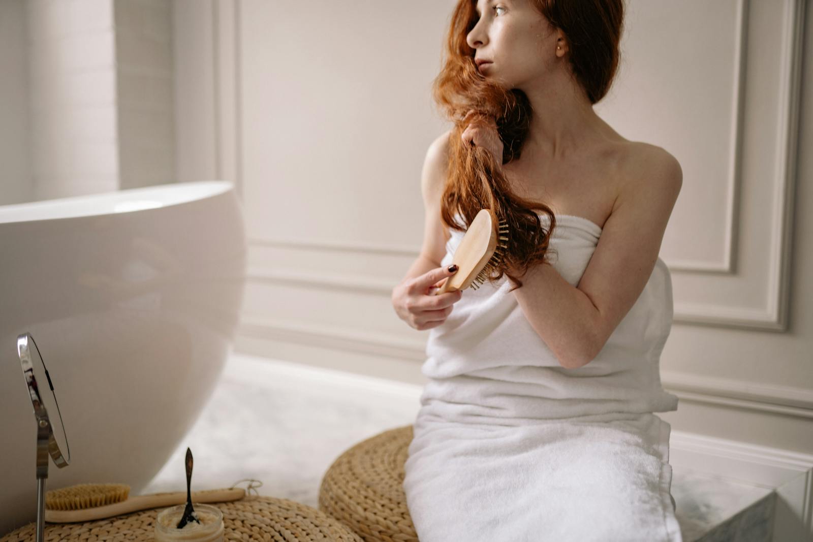 Woman wrapped in towel brushing hair in a modern indoor bathroom setting.