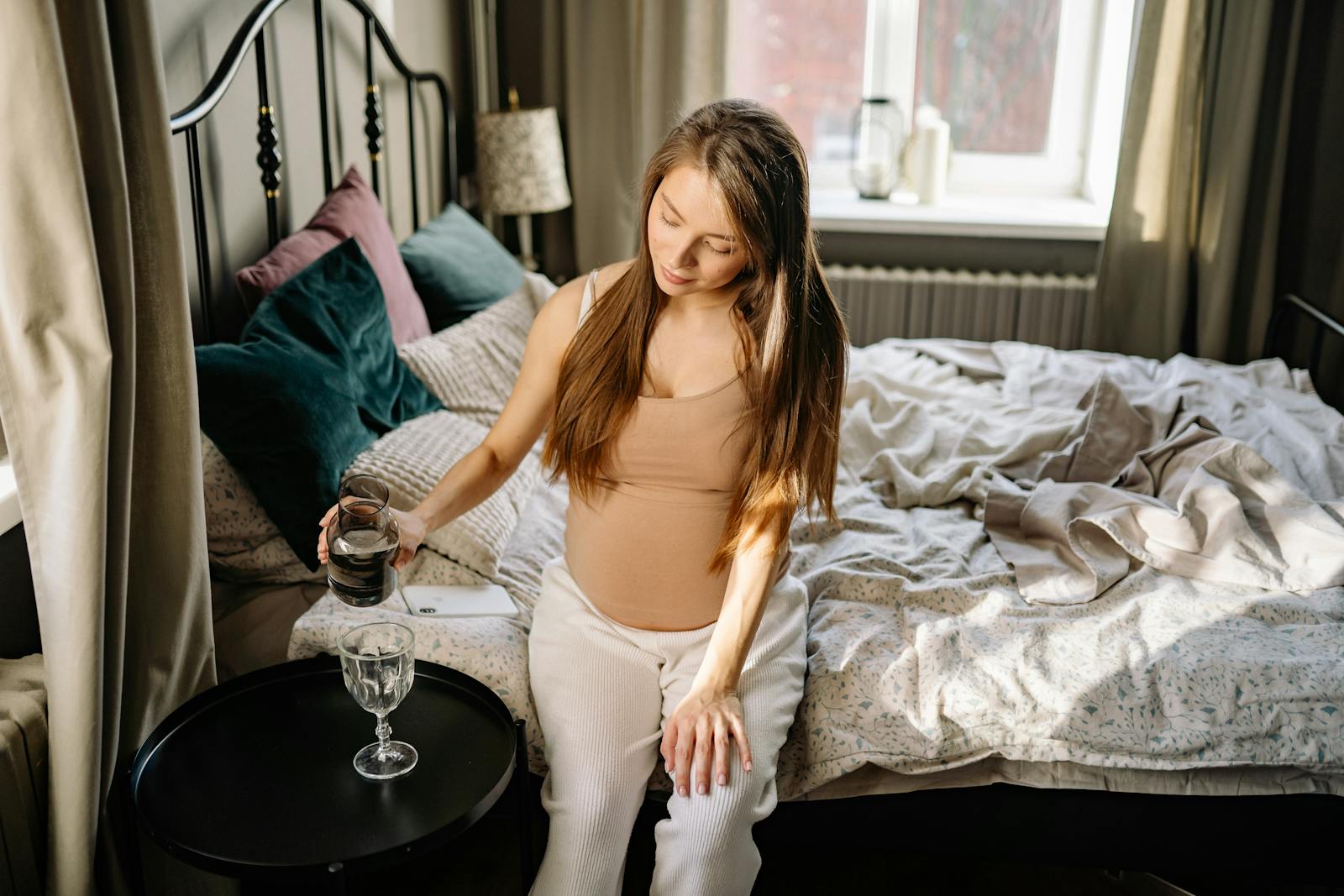 Caucasian woman sitting on bed, enjoying a calm moment during pregnancy.