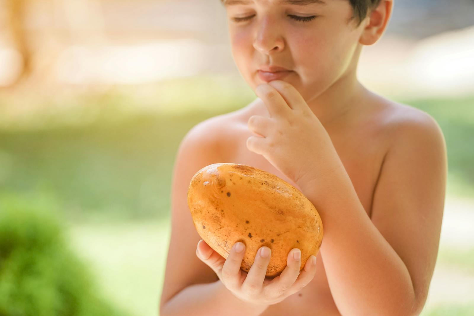 A young boy curiously inspects a fresh mango on a sunny summer day.