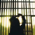 Silhouette of a woman stretching in front of large window blinds with sunlight streaming in.