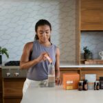 A woman uses essential oils and supplements in a contemporary kitchen for wellness.