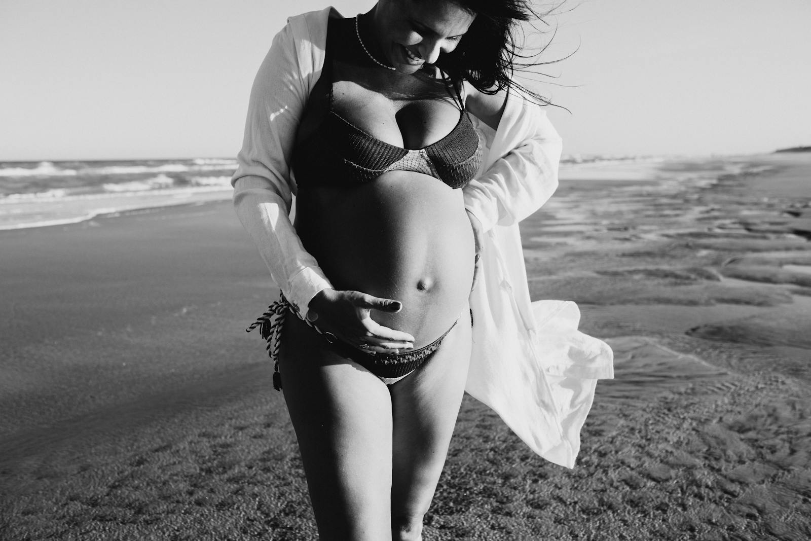 Monochrome photo of smiling expecting woman on beach capturing the joy of maternity.