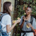 Two women hikers enjoying fresh fruit while backpacking outdoors, capturing a vibrant lifestyle moment.