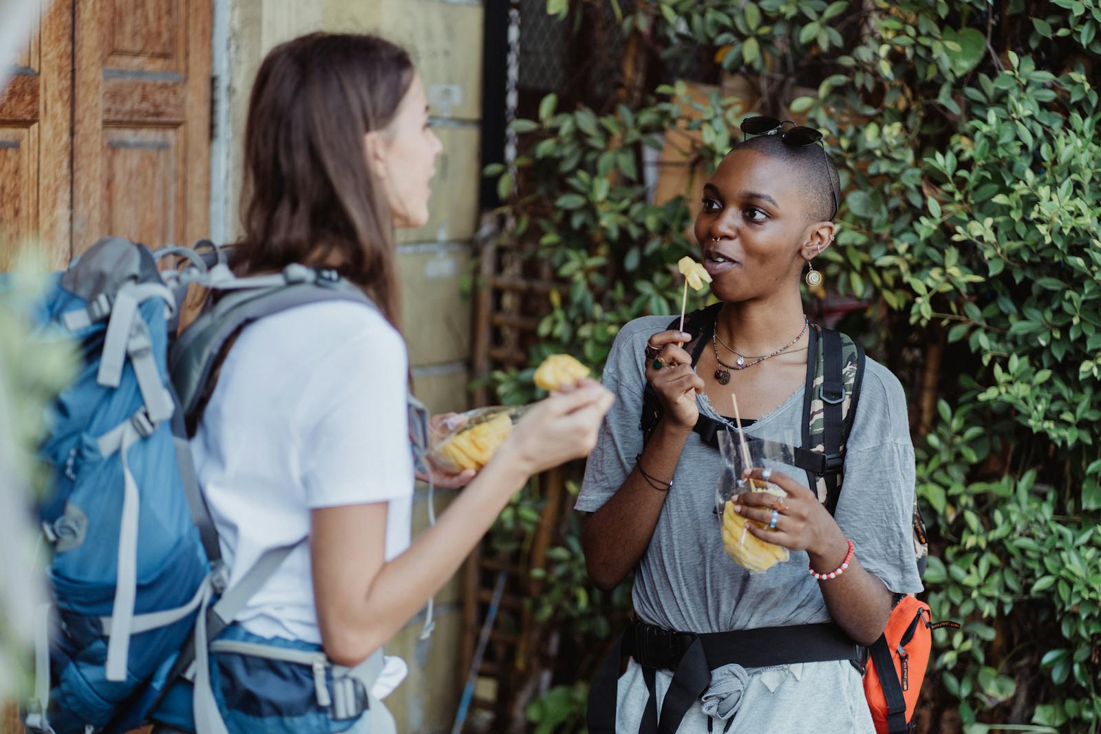Two women hikers enjoying fresh fruit while backpacking outdoors, capturing a vibrant lifestyle moment.