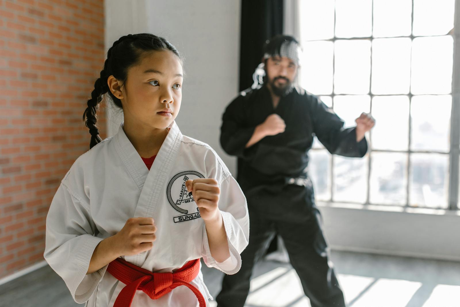 Young girl and instructor practicing martial arts in a well-lit dojo.